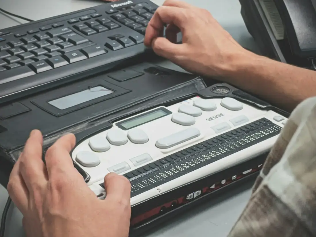 Hands on a refreshable braille display in front of a computer keyboard.